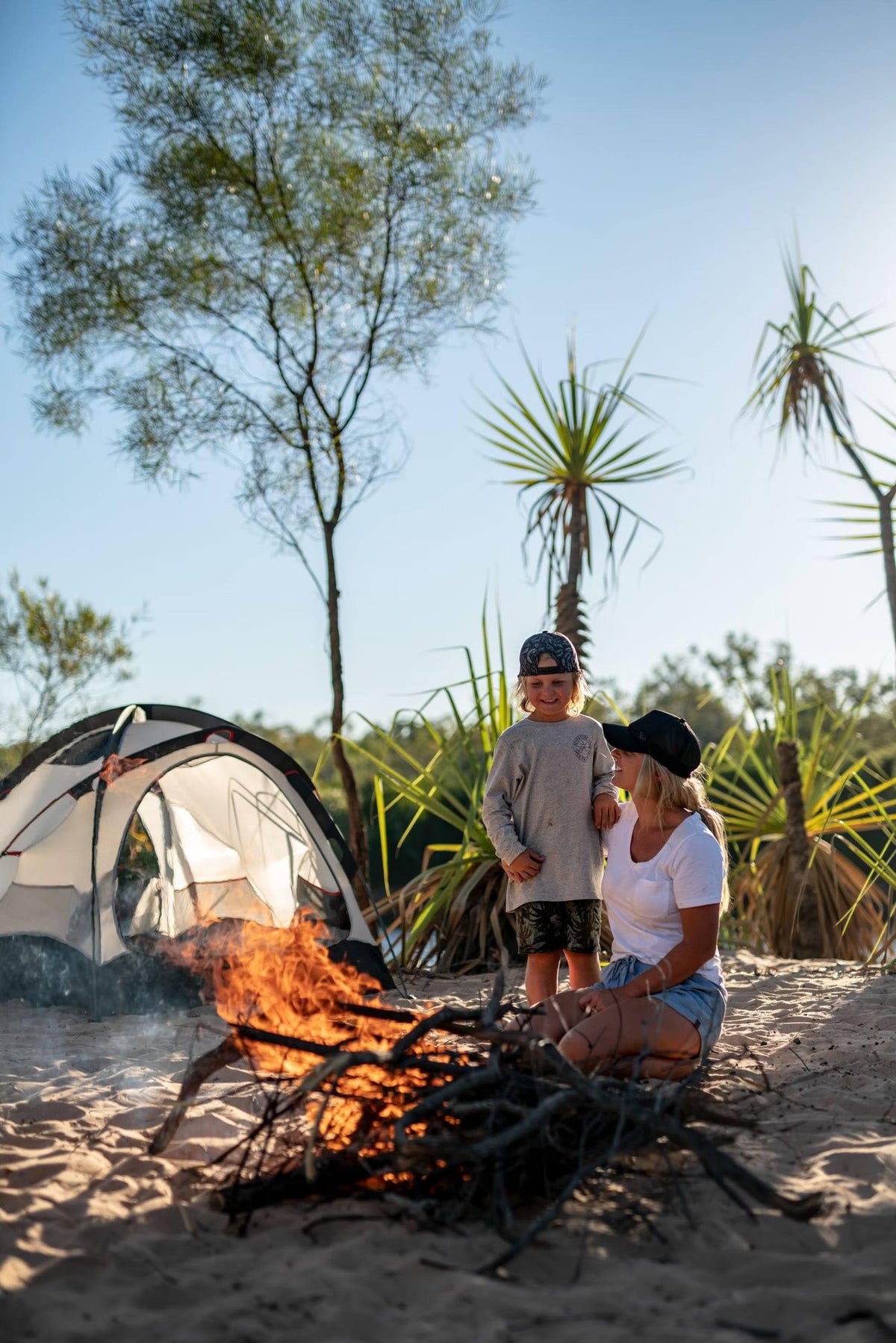 A mother and her son are lighting a bonfire next to their campsite.