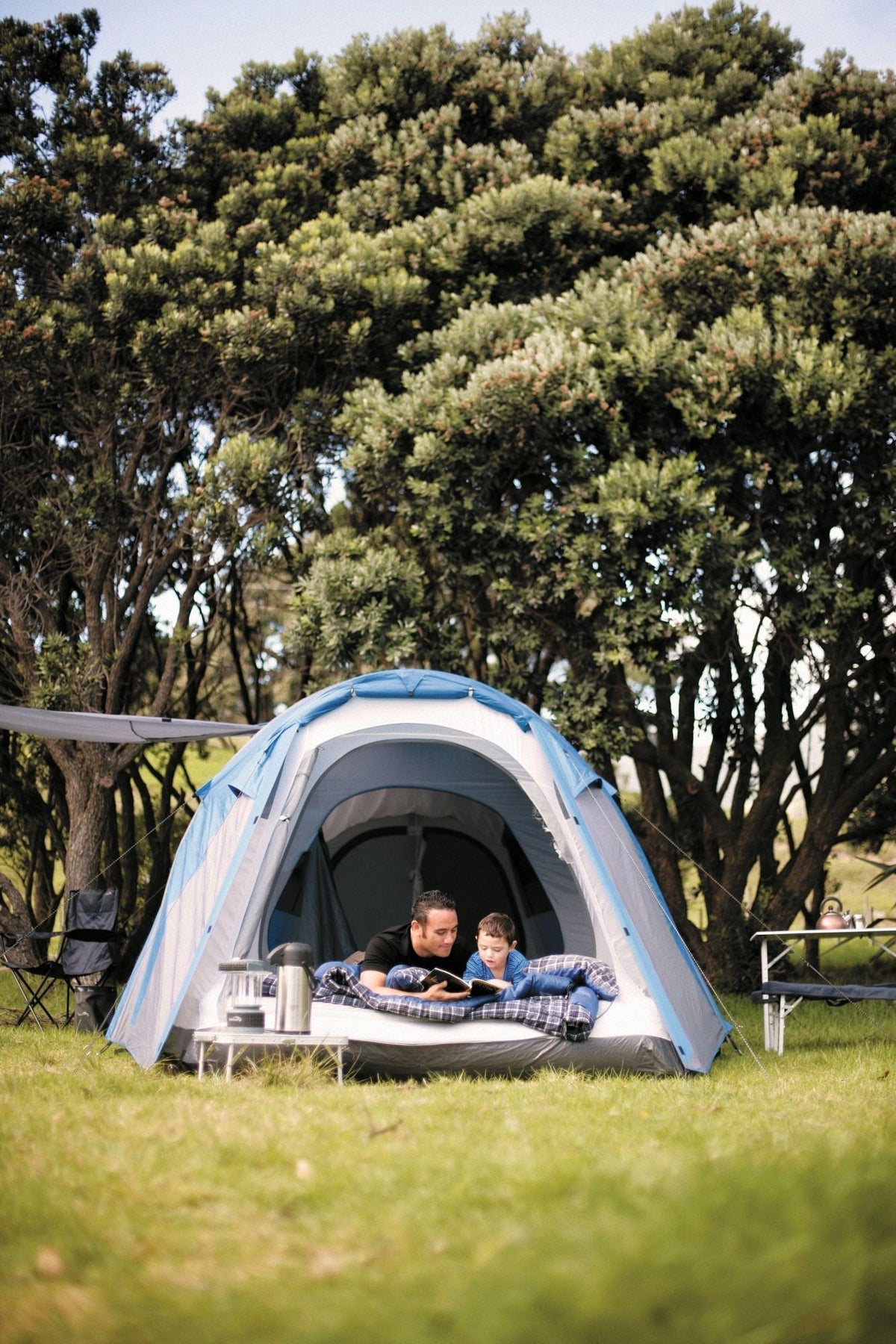 Father and son reading a book together at their campsite