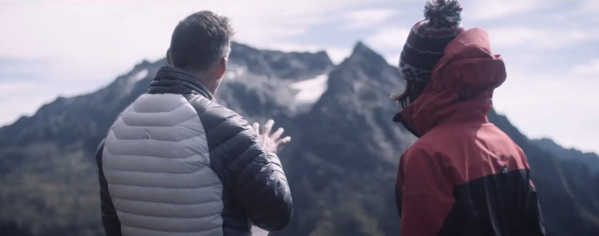 Tim Jarvis in conversation with a second person. Both are facing away from the camera towards a mountain range.