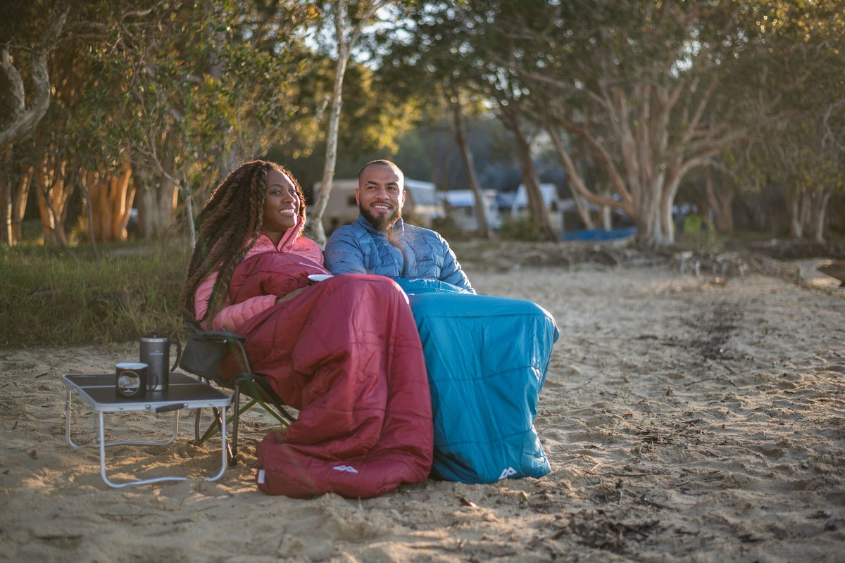 A couple is enjoying a morning coffee wrapped in their down sleeping bags.
