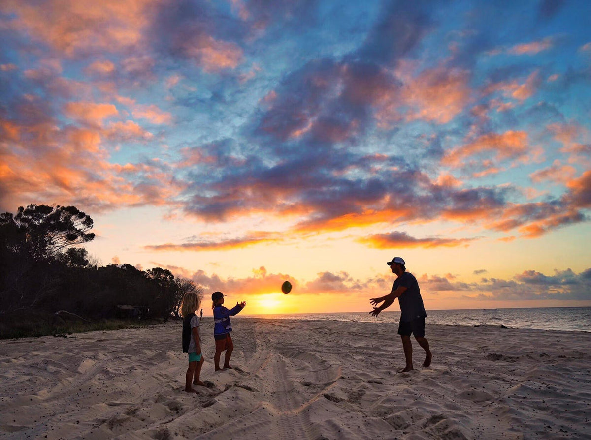Dad playing football on the beach with his two kids at sun set.