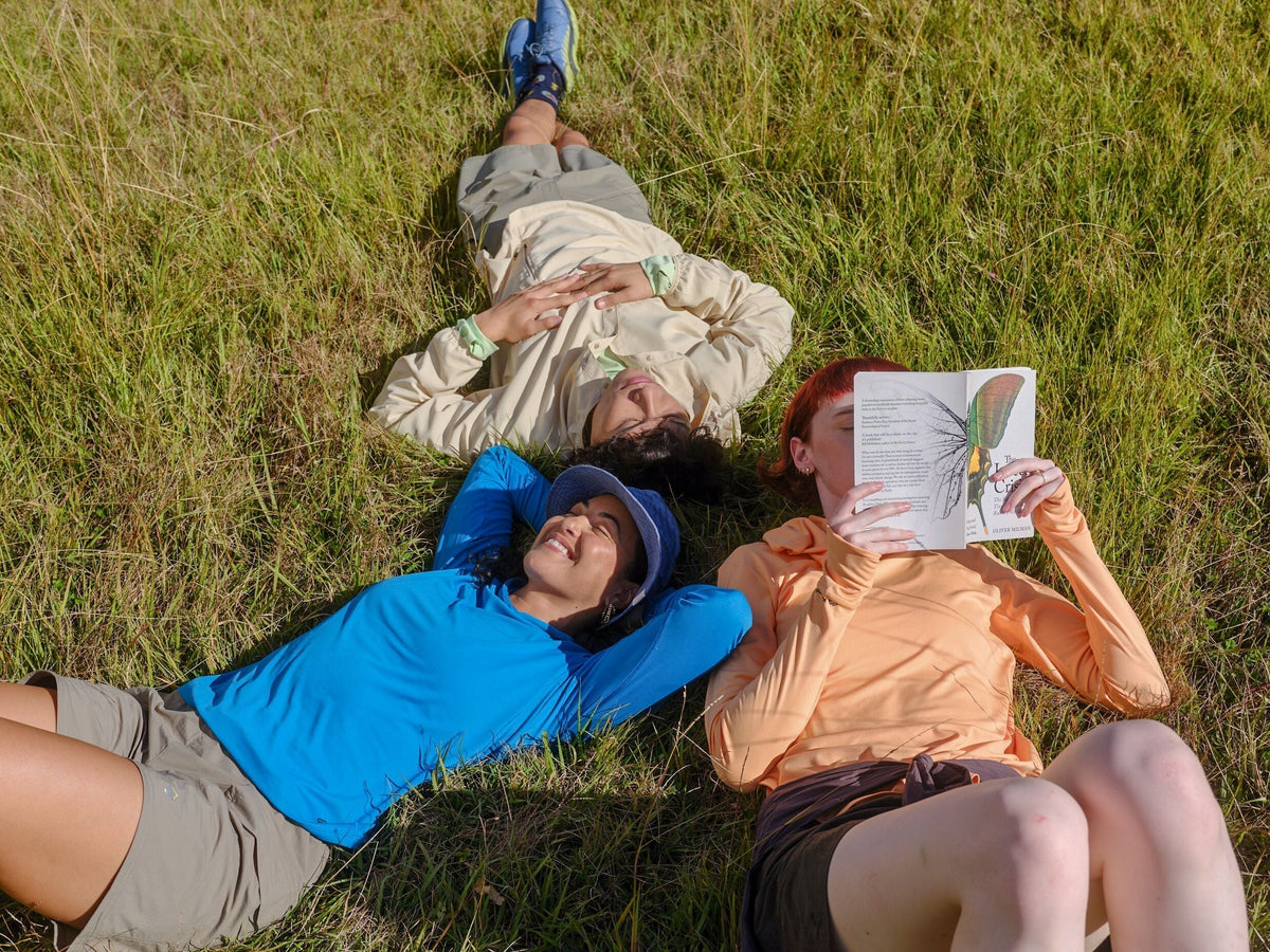 Three friends are relaxing in the grass in the sun wearing Kathmandu UPF clothing